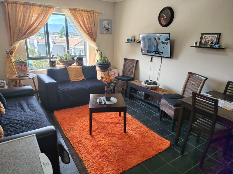 A comfortable living room featuring dark tiled flooring, a large window with natural light, and wall-mounted television connectivity.