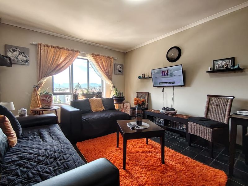 A comfortable living room featuring tiled flooring, coved ceilings, and a large window providing natural light and scenic views.