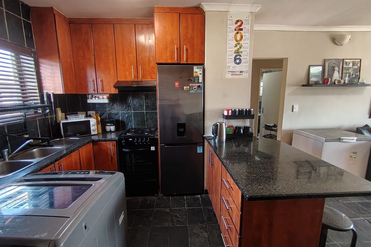 A functional kitchen featuring wooden cabinetry, granite countertops, a gas stove with extractor, and a breakfast nook, finished with slate tile flooring.