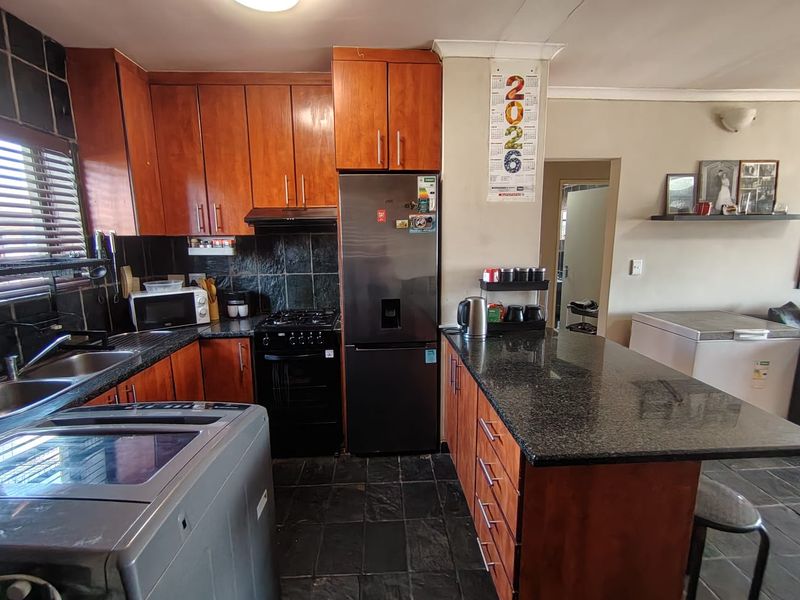 A functional kitchen featuring wooden cabinetry, granite countertops, a gas stove with extractor, and a breakfast nook, finished with slate tile flooring.