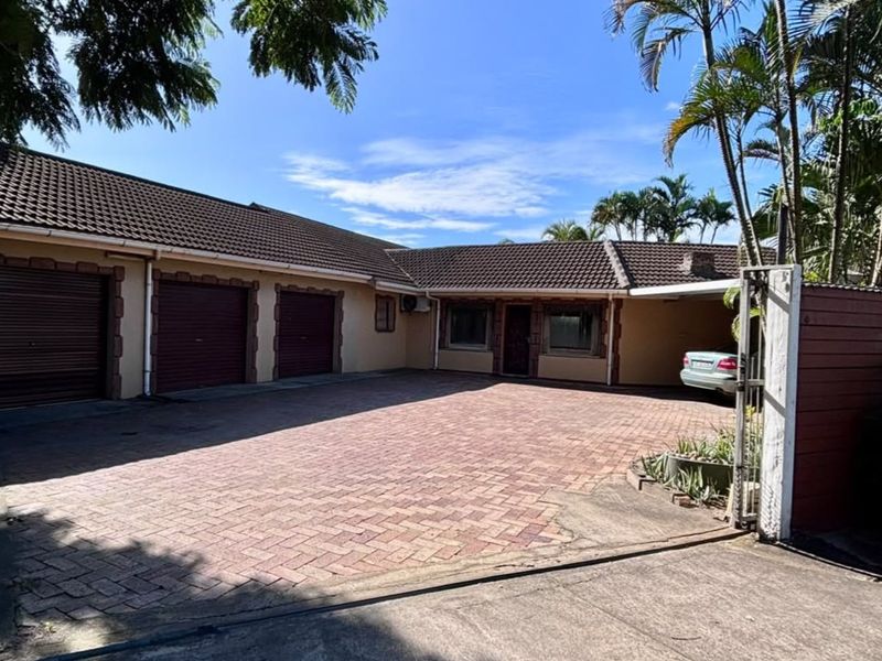 Front exterior view of the property featuring a spacious paved driveway, triple garage, and a covered carport area.