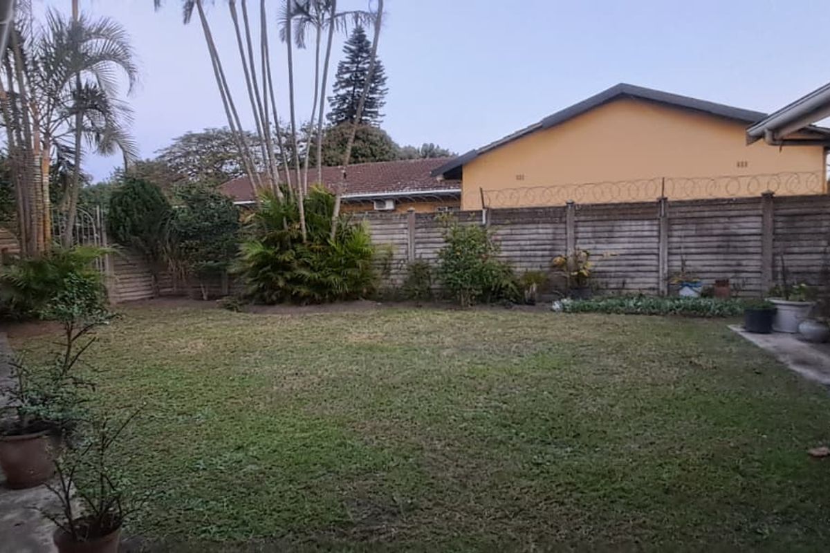 A private rear garden featuring a lawn area, paved walkways, and a secure perimeter wall topped with razor wire.