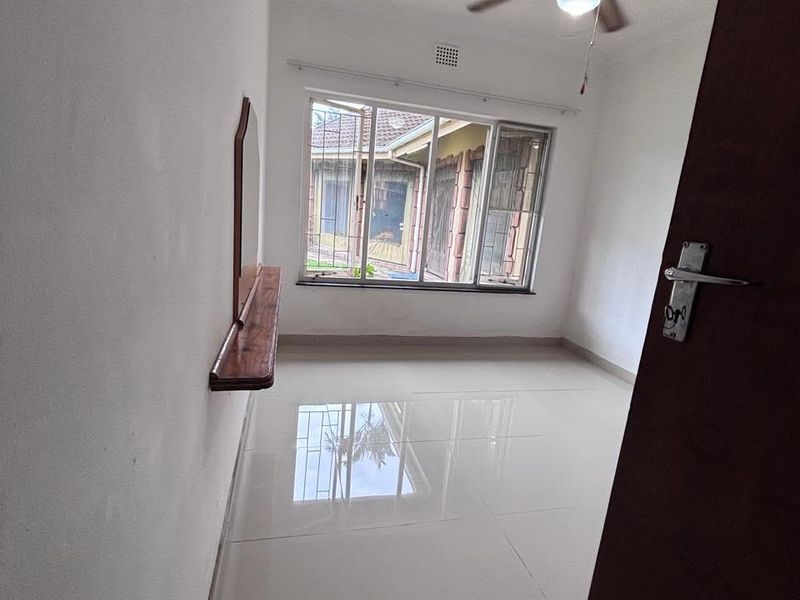A bright, empty bedroom featuring polished tiled flooring, a ceiling fan, and a built-in wall shelf with a window overlooking the exterior.