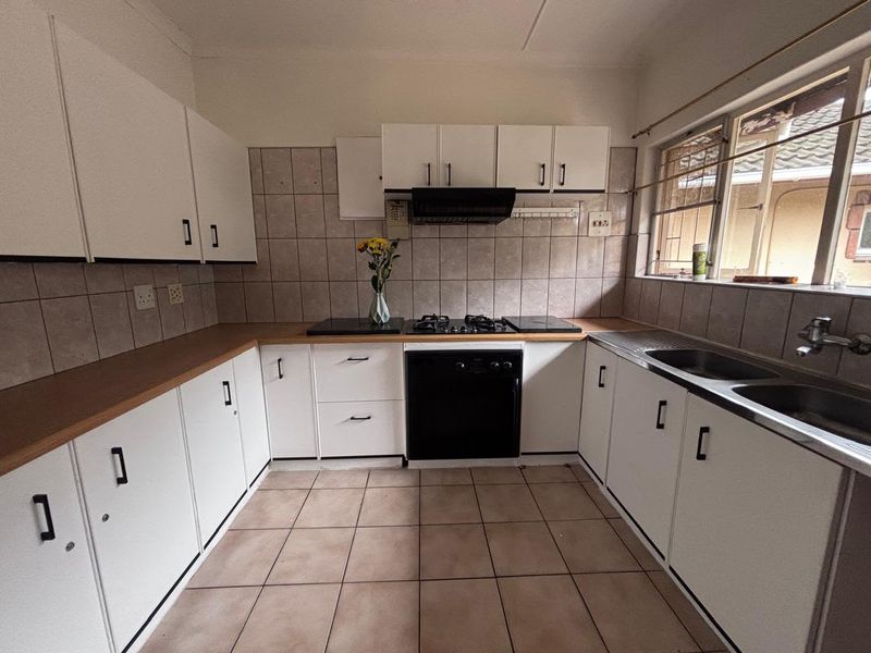 Functional kitchen featuring white cabinetry, gas hob, built-in oven, extractor fan, and tiled splashback with ample counter space.