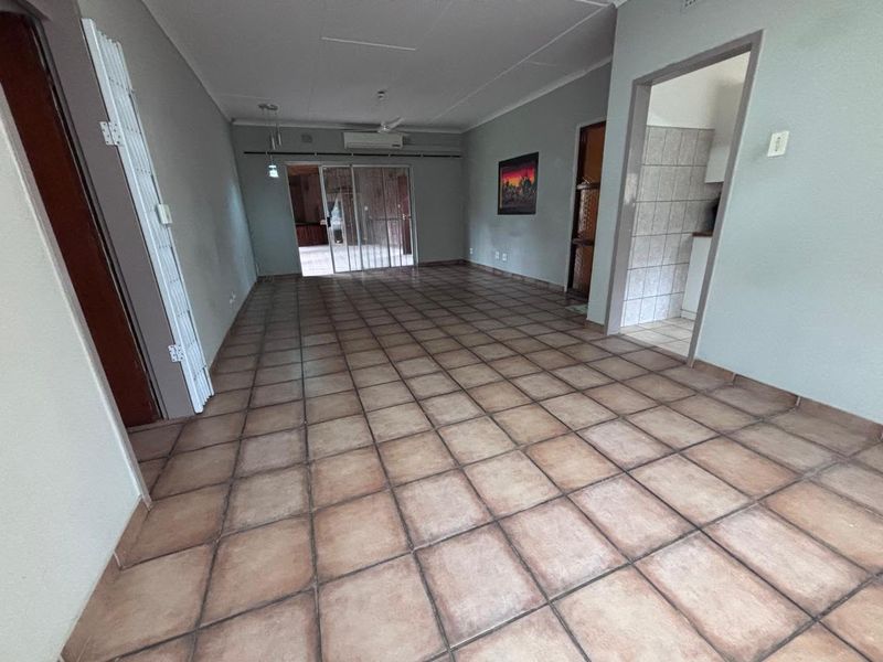 Spacious open-plan living area featuring neutral tiled flooring, an air conditioning unit, and direct access to an outdoor patio through sliding glass doors.