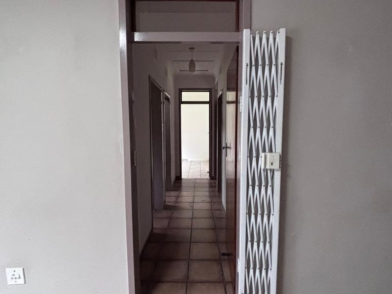 A vacant hallway featuring tiled flooring and a white security gate, providing access to multiple rooms within the property.