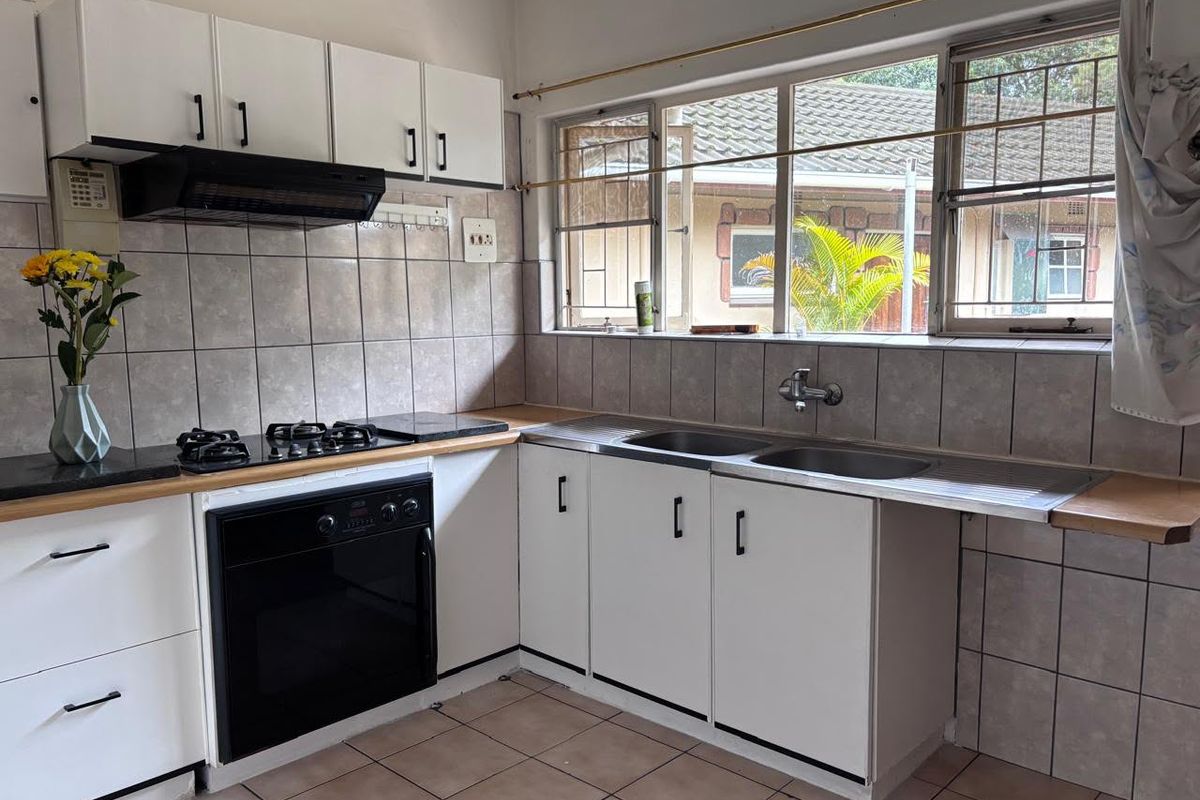 Functional kitchen featuring white cabinetry, gas hob, built-in oven, extractor fan, and double stainless steel sink with tiled splashback and flooring.