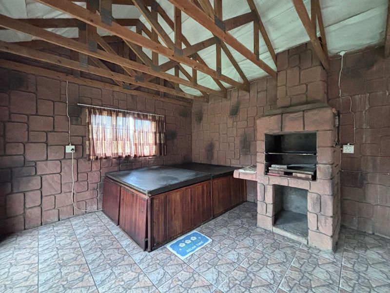Covered patio area featuring exposed timber roof trusses, stone-clad walls, and a built-in braai, offering a rustic outdoor entertainment space.