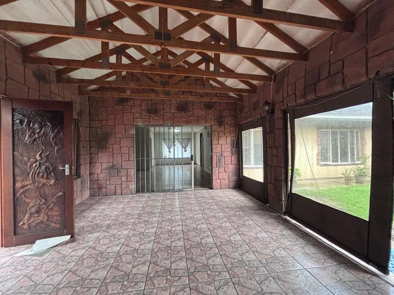 Covered patio area featuring exposed timber roof trusses, stone-effect wall cladding, tiled flooring, and roll-up outdoor blinds, providing a versatile outdoor entertainment space.