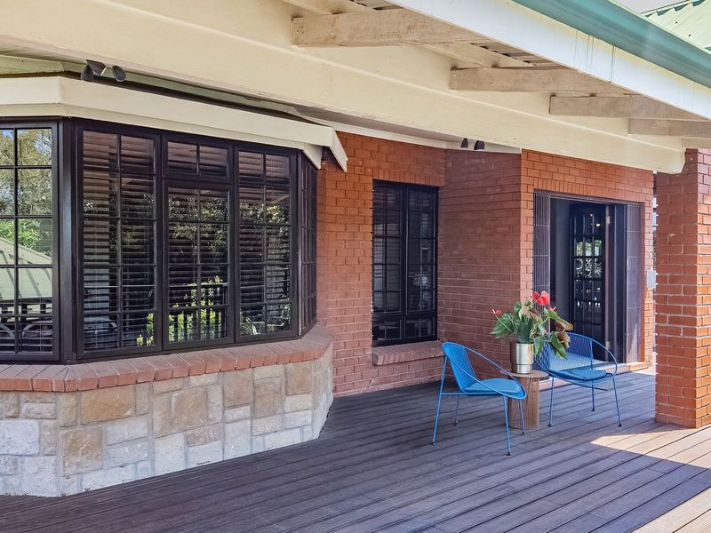 A spacious covered patio featuring timber decking, exposed rafters, and a combination of brick and stone exterior finishes with a large bay window.