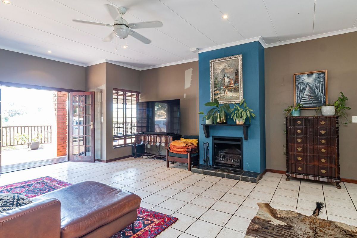 Spacious living room featuring tiled flooring, a central fireplace with a blue accent wall, ceiling fan, and direct access to an outdoor balcony.