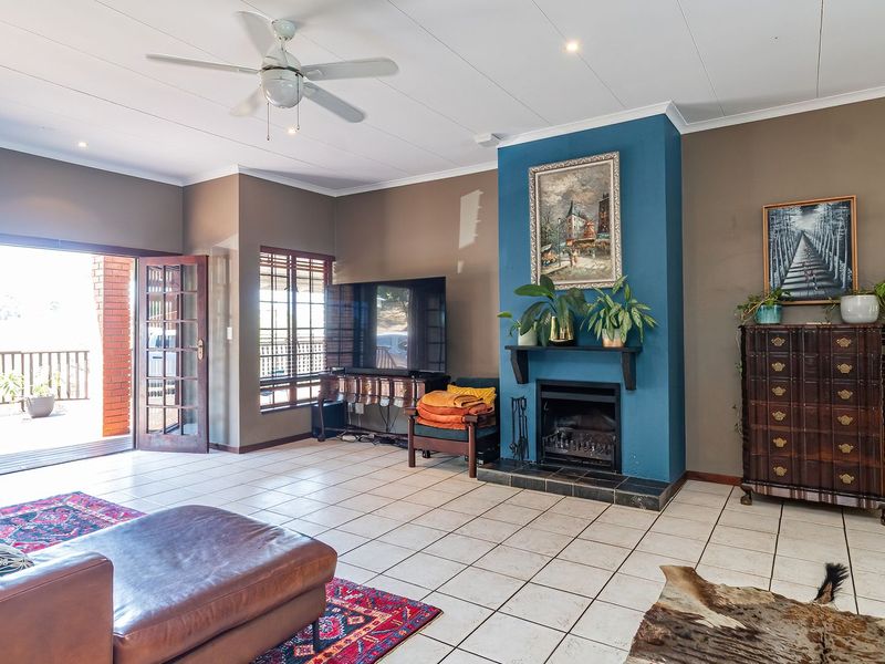 Spacious living room featuring tiled flooring, a central fireplace with a blue accent wall, ceiling fan, and direct access to an outdoor balcony.