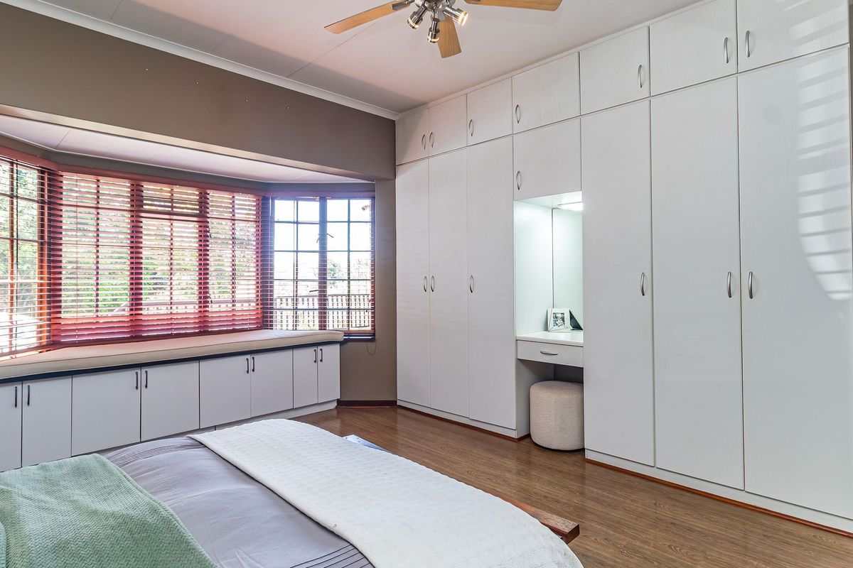 Spacious bedroom featuring extensive built-in cabinetry, an integrated vanity, and a large bay window with a built-in storage seat and laminate flooring.