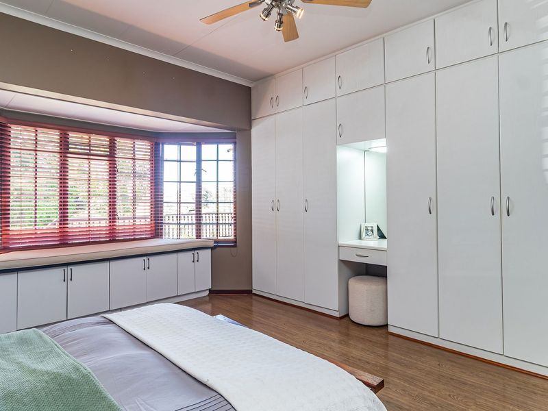 Spacious bedroom featuring extensive built-in cabinetry, an integrated vanity, and a large bay window with a built-in storage seat and laminate flooring.