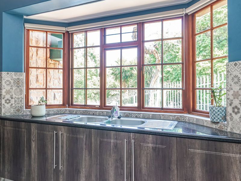 A well-maintained kitchen area featuring a large bay window, dark wood-grain cabinetry, granite countertops, and decorative patterned tile backsplash.