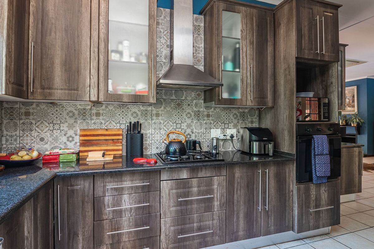 Modern kitchen featuring dark wood-grain cabinetry, granite countertops, a gas hob with stainless steel extractor, and a decorative patterned tile backsplash.