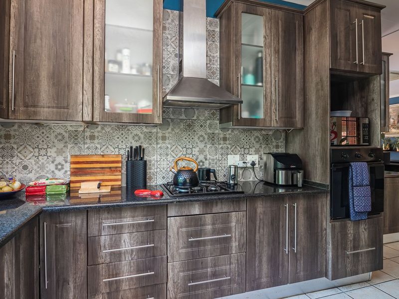 Modern kitchen featuring dark wood-grain cabinetry, granite countertops, a gas hob with stainless steel extractor, and a decorative patterned tile backsplash.