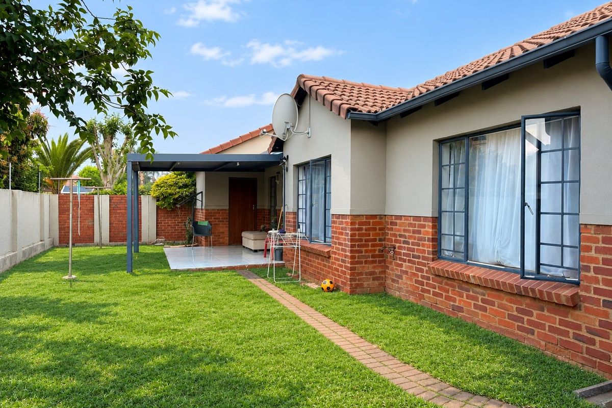 Rear view of the townhouse featuring a well-maintained garden, a covered patio area, and a combination of brick and plastered exterior finishes.