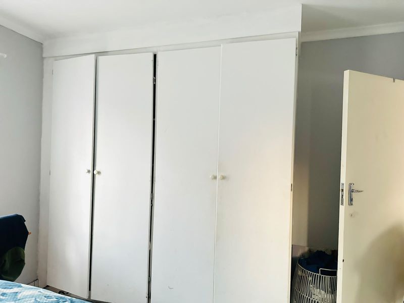 A bedroom featuring white built-in cupboards with classic hardware and ceiling cornicing.
