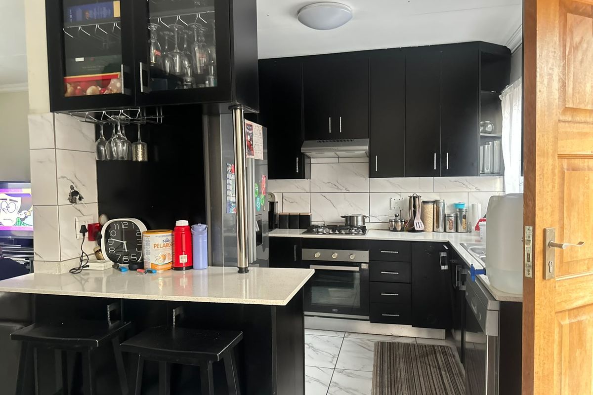 Modern kitchen featuring black cabinetry, stone countertops, marble-look wall tiles, and a functional breakfast bar with integrated gas hob and oven.