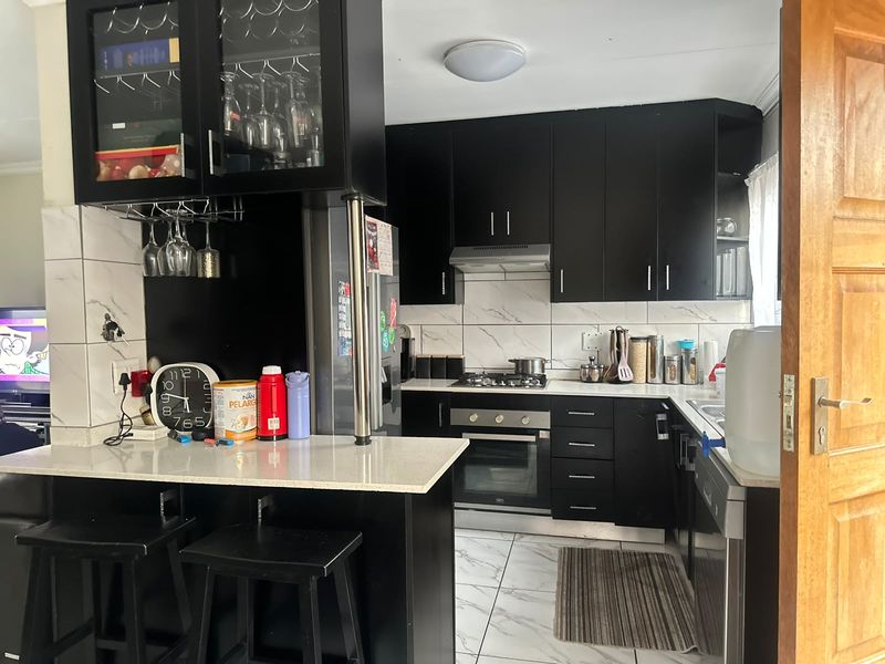 Modern kitchen featuring black cabinetry, stone countertops, marble-look wall tiles, and a functional breakfast bar with integrated gas hob and oven.