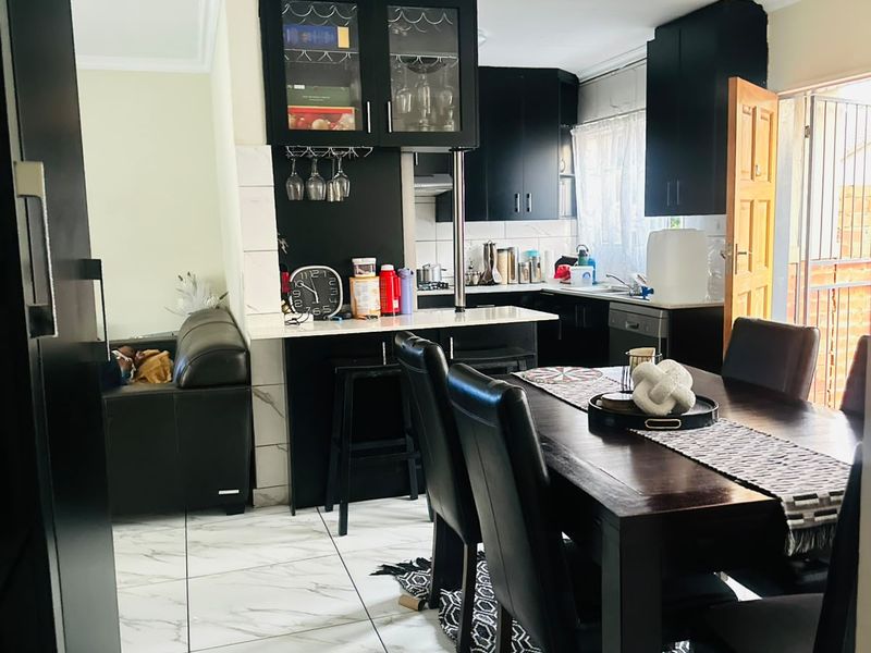 Open-plan kitchen and dining area featuring modern black cabinetry, marble-look tiled flooring, and a breakfast bar, creating a functional and cohesive living space.