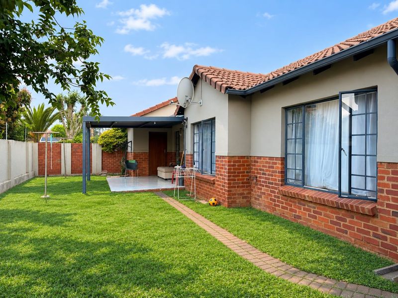 Rear view of the townhouse featuring a well-maintained garden, a covered patio area, and a combination of brick and plastered exterior finishes.