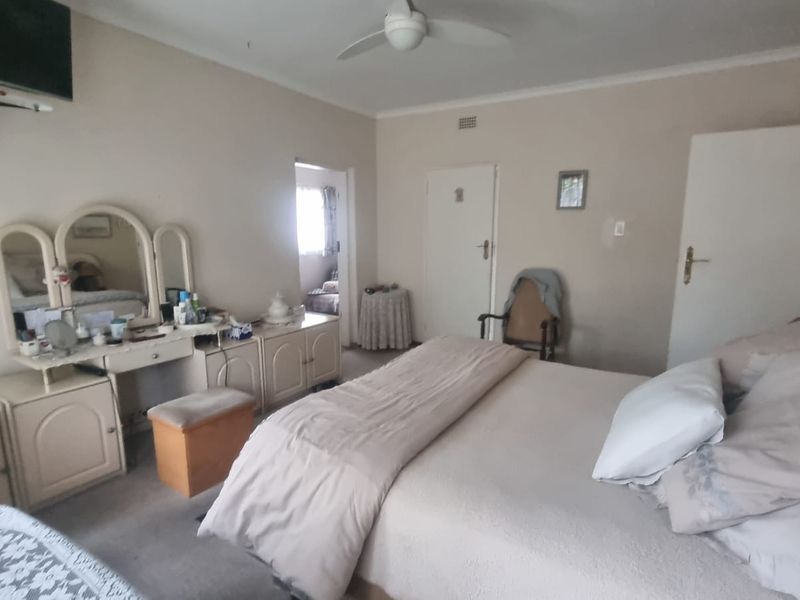 A spacious bedroom featuring neutral wall tones, a ceiling fan, and multiple access doors, offering a functional layout ready for modern updates.