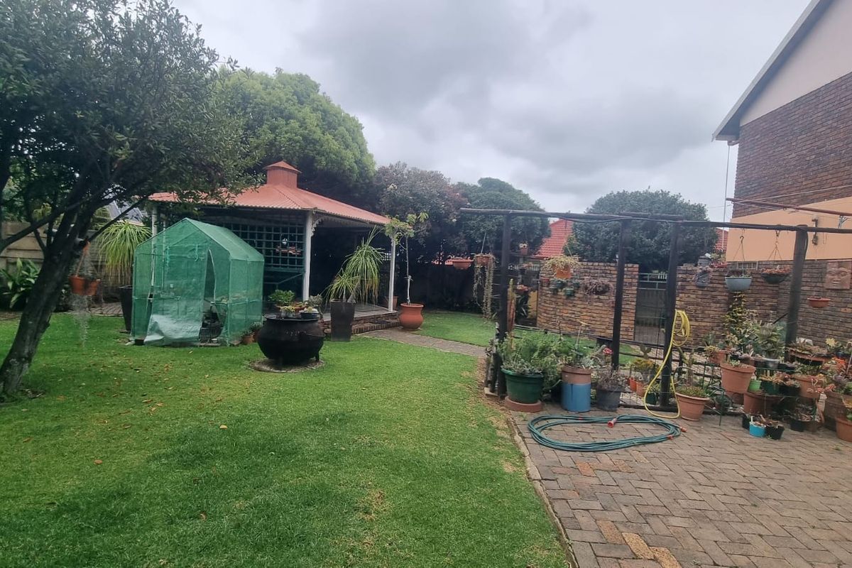 A spacious rear garden featuring a paved patio area, a covered gazebo, and a timber pergola, set against a brick boundary wall.