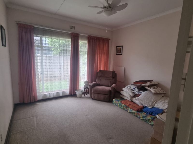 A bedroom featuring carpeted flooring, a ceiling fan, and a large window providing natural light.