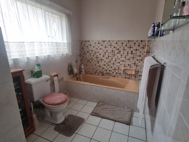 A functional bathroom featuring a built-in bathtub, ceramic tiling, and standard sanitary ware, offering a dated aesthetic ready for modernization.