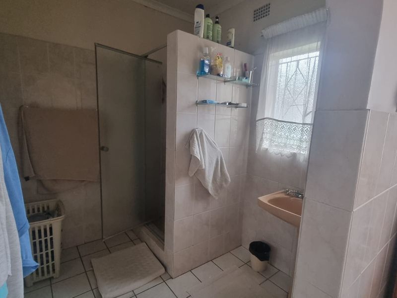 A functional bathroom featuring a shower enclosure, wall-mounted basin, and tiled finishes. The space would benefit from modern updates to fixtures and tiling.