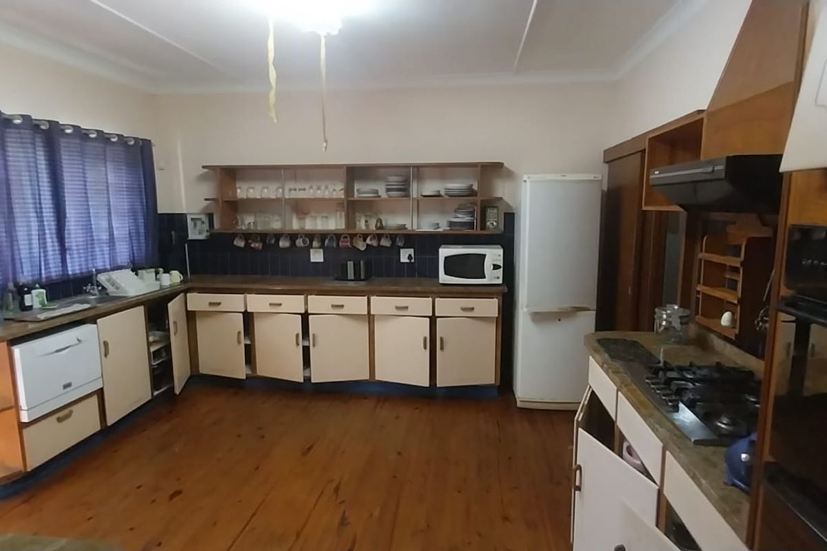 A spacious kitchen featuring timber flooring, built-in cabinetry, a gas hob with extractor, and a tiled splashback, offering a functional layout with dated finishes.