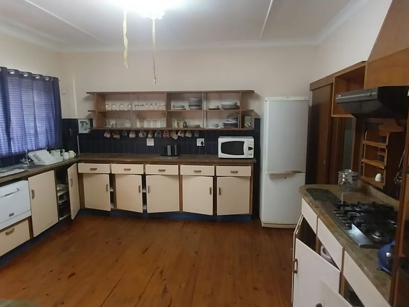 A spacious kitchen featuring timber flooring, built-in cabinetry, a gas hob with extractor, and a tiled splashback, offering a functional layout with dated finishes.