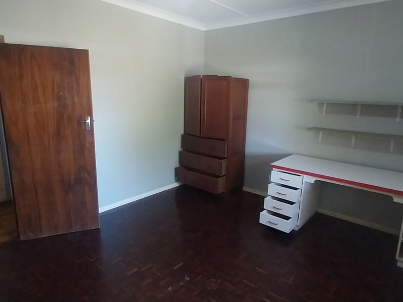 A bedroom featuring dark parquet flooring, built-in desk with drawers, and wall-mounted shelving, offering a functional space with potential for modernization.