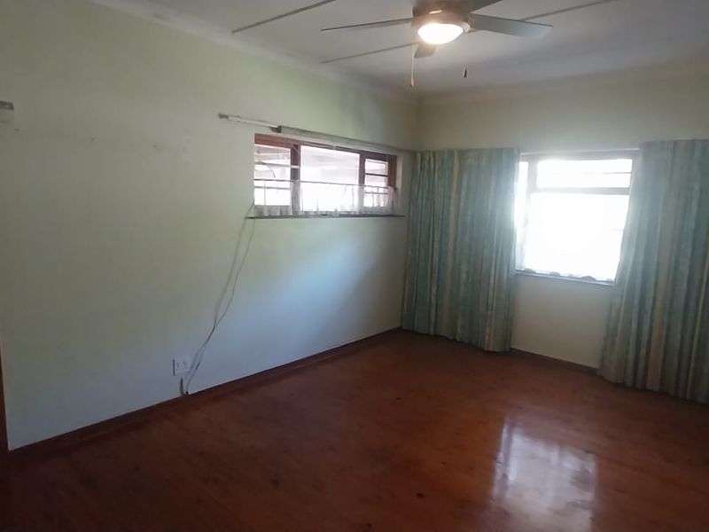 An empty bedroom featuring timber flooring, a ceiling fan, and natural light through multiple windows.