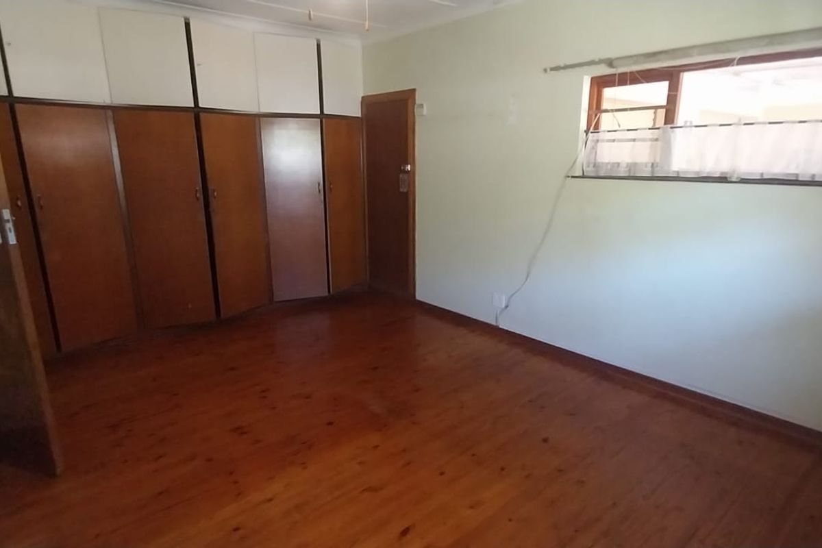 A spacious bedroom featuring original timber flooring and extensive built-in cabinetry, offering a blank canvas for renovation or modern styling.