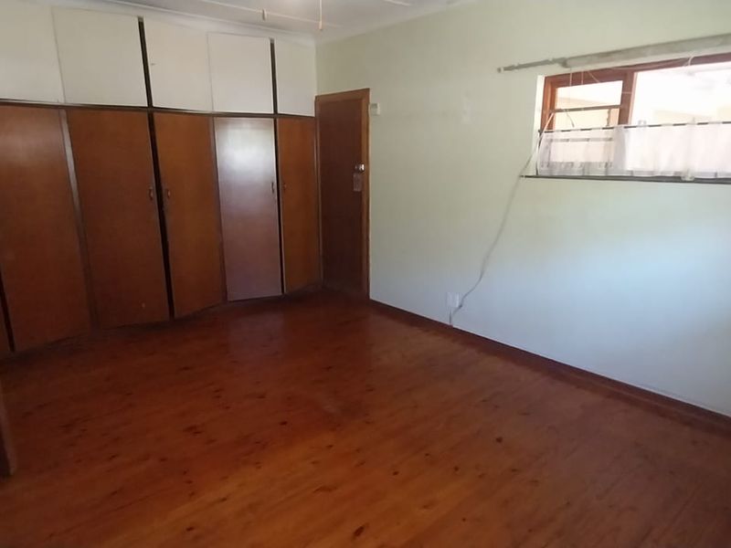 A spacious bedroom featuring original timber flooring and extensive built-in cabinetry, offering a blank canvas for renovation or modern styling.