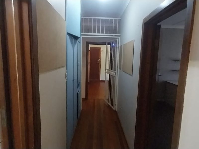 A narrow hallway featuring timber flooring, built-in storage cupboards, and a security gate, providing access to adjacent rooms.
