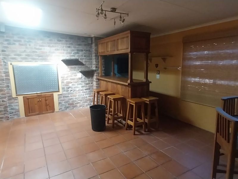A dedicated bar area featuring a built-in wooden bar counter, exposed brick feature wall, and tiled flooring with access to an outdoor area.
