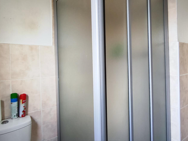 A functional bathroom featuring a shower enclosure with frosted glass doors and neutral ceramic wall tiling.