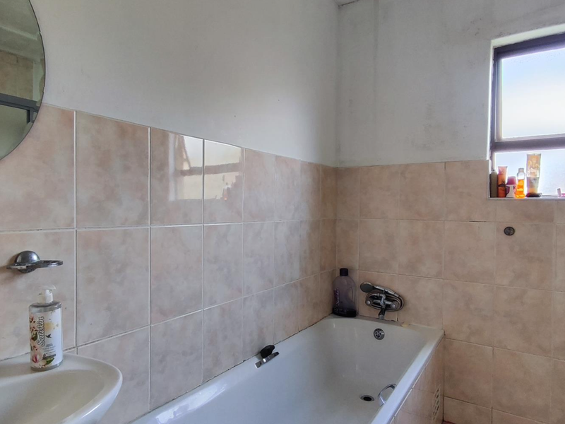 A functional bathroom featuring a bathtub, basin, and tiled walls. The space would benefit from cosmetic updates to the ceiling and wall finishes.