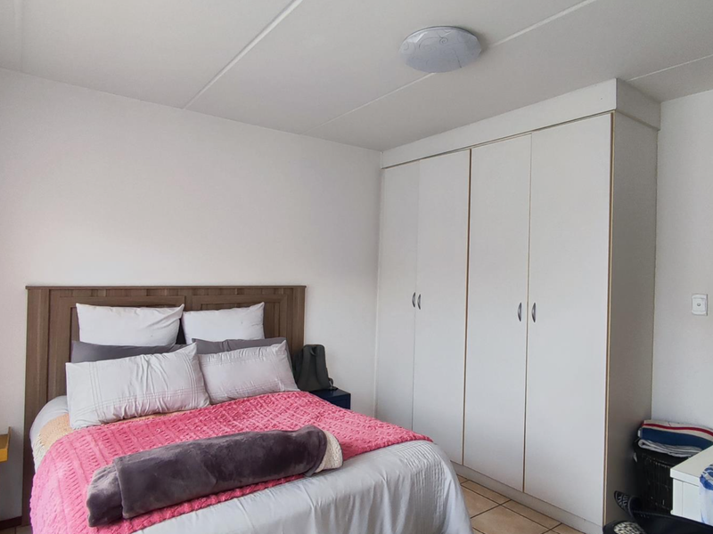 A functional bedroom featuring built-in cupboards, tiled flooring, and a neutral color palette, offering a clean and practical living space.