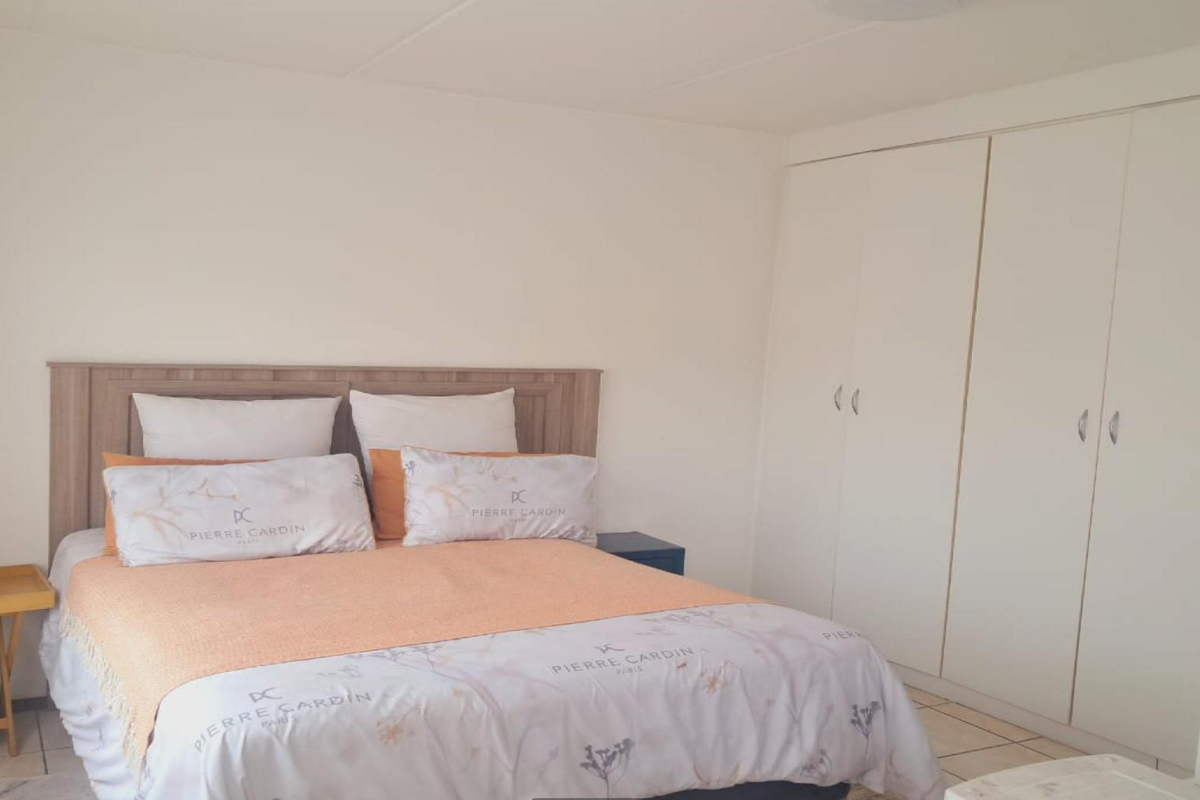 A bedroom featuring neutral walls, tiled flooring, and a large built-in wardrobe providing ample storage space.