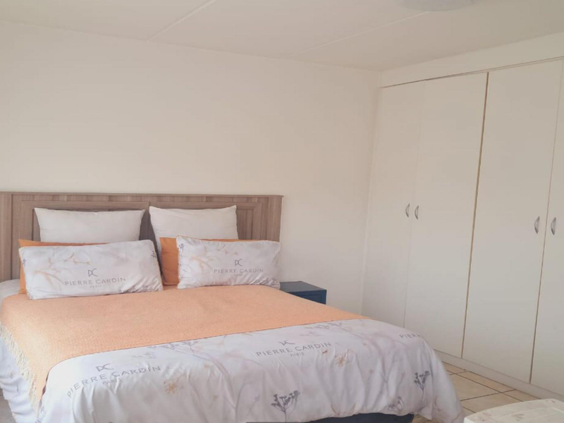 A bedroom featuring neutral walls, tiled flooring, and a large built-in wardrobe providing ample storage space.