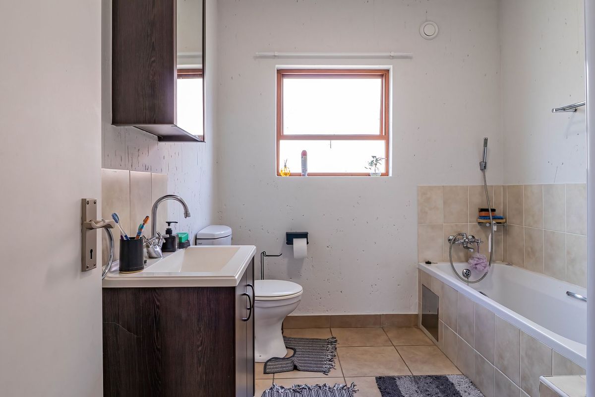 A functional bathroom featuring a vanity cabinet, toilet, and a bathtub with a shower mixer, finished with tiled flooring and splashbacks.