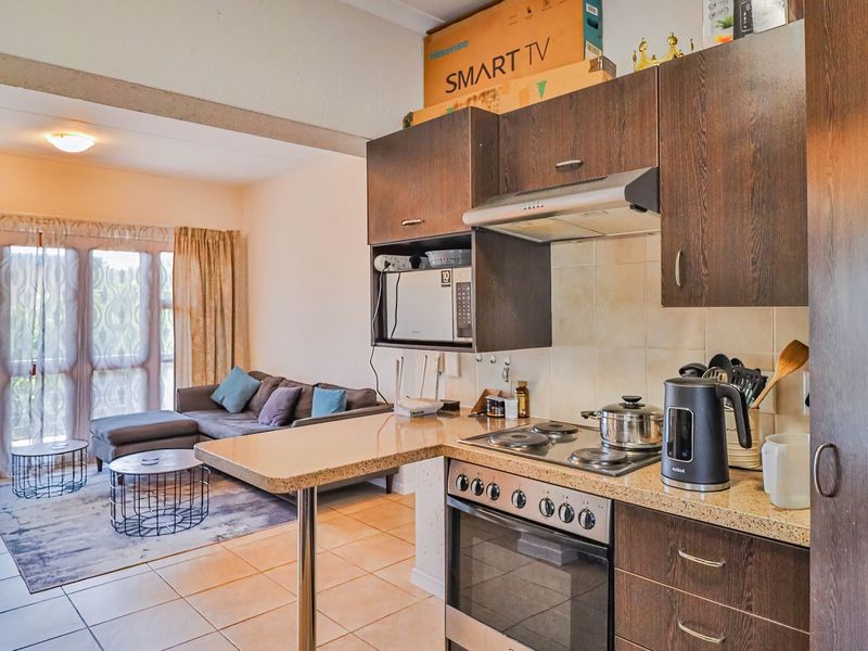 Open-plan living area featuring a compact kitchen with built-in cabinetry, electric hob, oven, and tiled flooring, leading to a bright lounge with sliding doors.