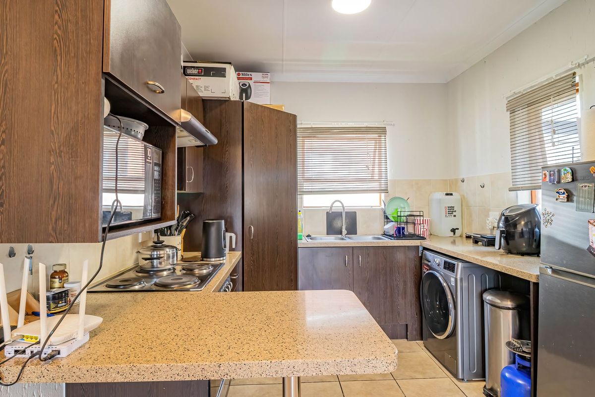 A functional kitchen featuring dark wood-look cabinetry, stone-effect countertops, a built-in electric hob, and integrated laundry plumbing, offering a practical layout for daily use.