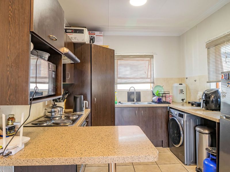 A functional kitchen featuring dark wood-look cabinetry, stone-effect countertops, a built-in electric hob, and integrated laundry plumbing, offering a practical layout for daily use.