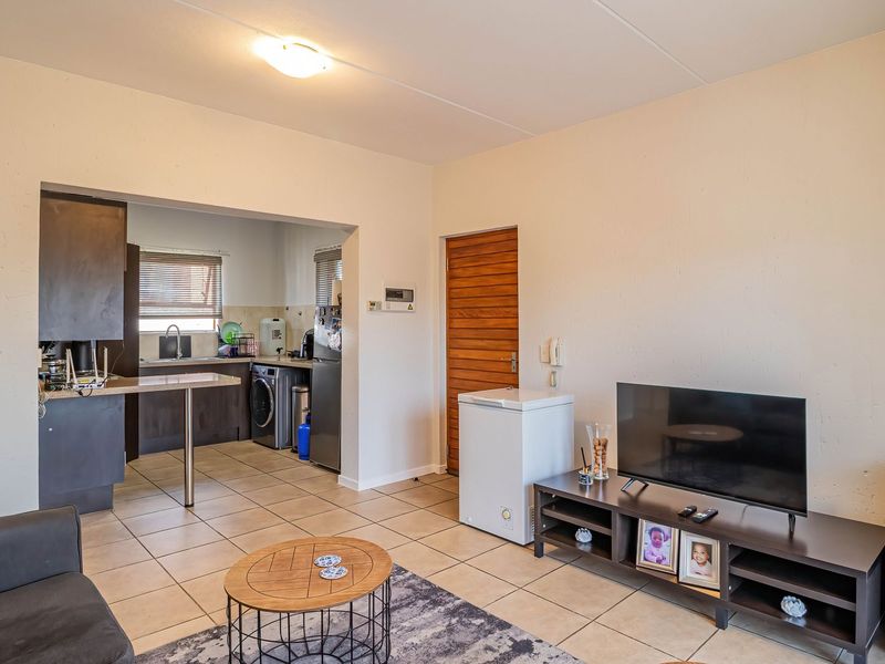 Open plan living area featuring tiled floors and an adjoining kitchen and laundry space with built-in cabinetry and sink.